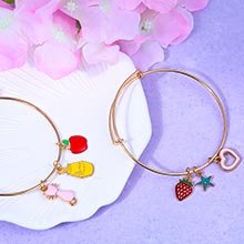 Two gold-tone bangle bracelets with colorful enamel charms including a strawberry, heart, star, apple, and bottle.