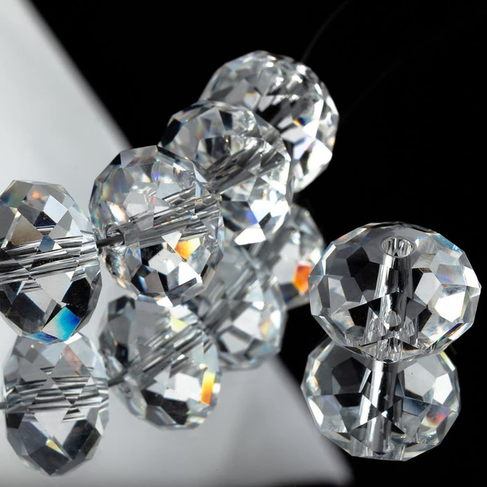 Clear faceted glass rondelle beads on a string, reflecting light against a black and white background.