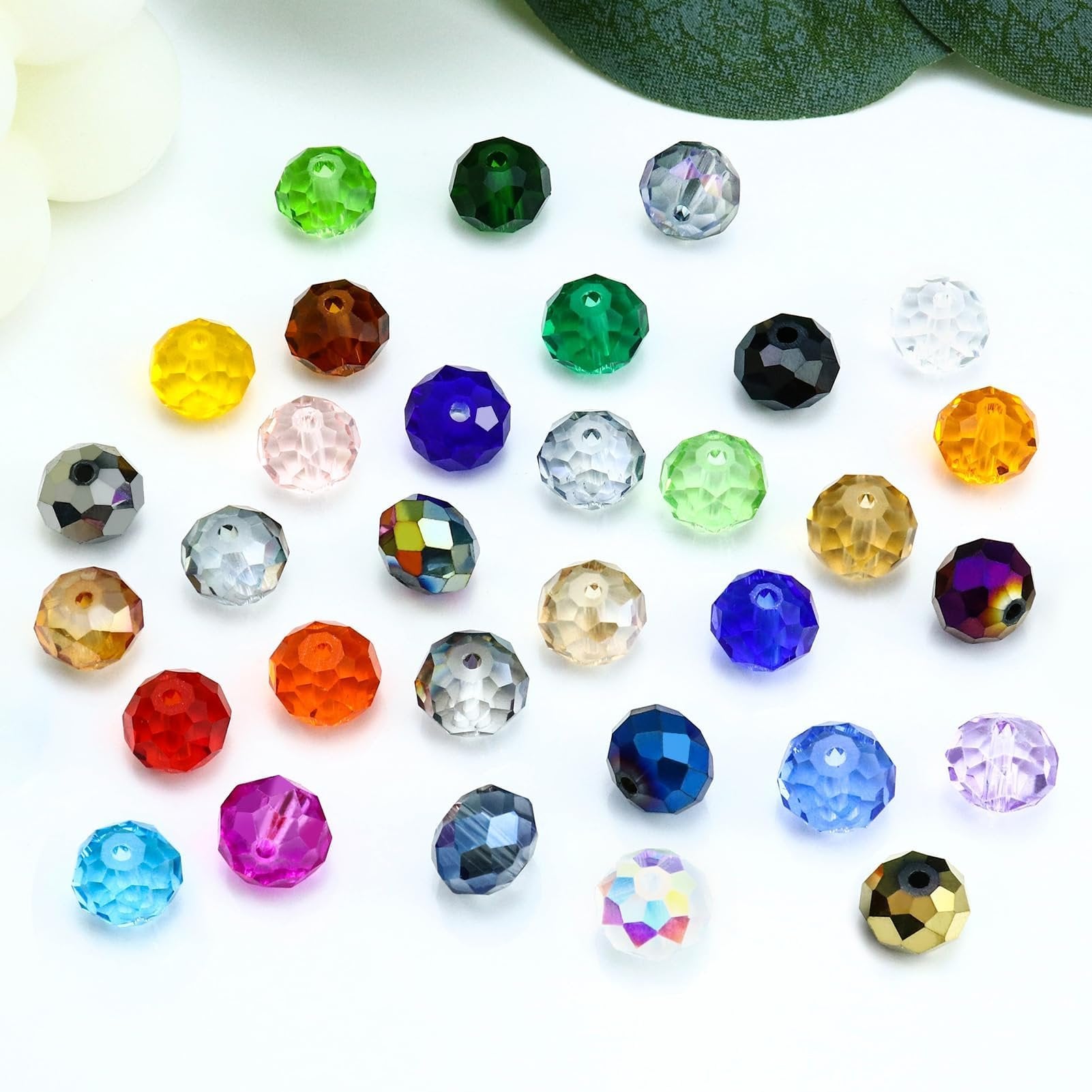 Assortment of faceted crystal glass beads in various colors including clear, blue, green, yellow, red, and purple, scattered on a white surface.