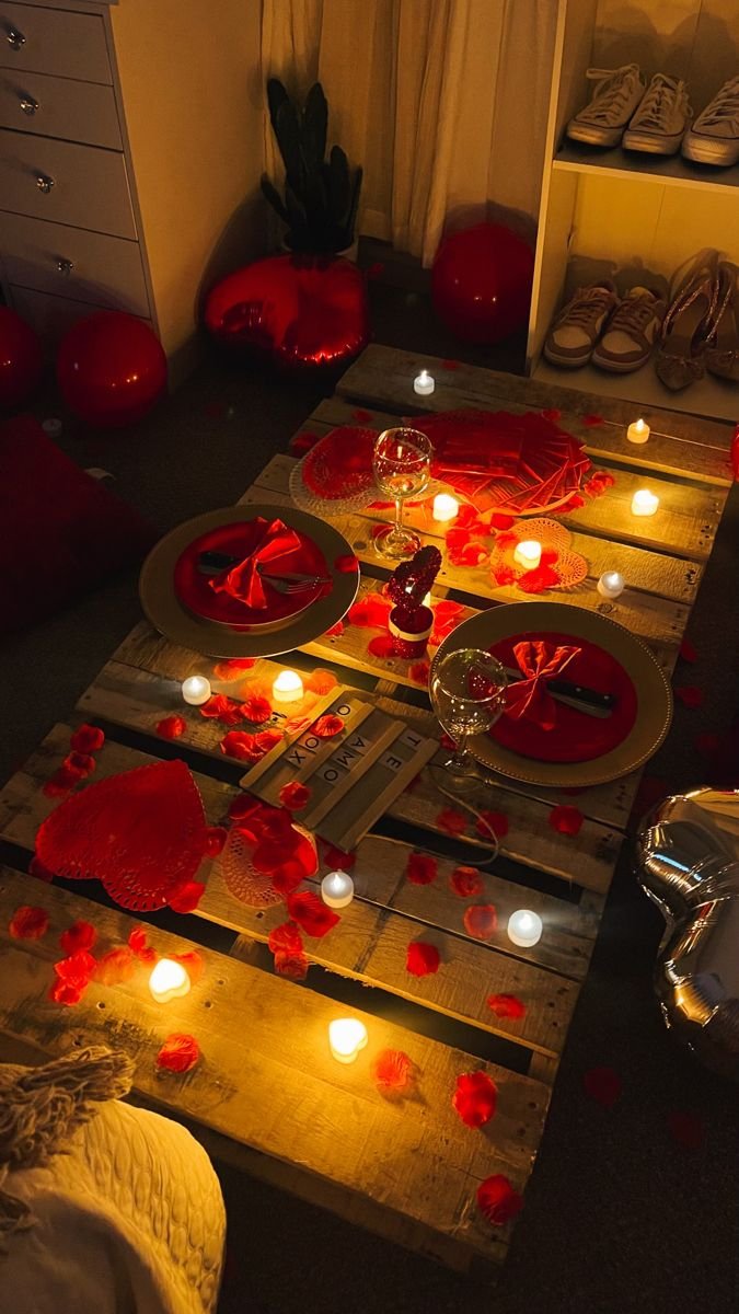 Romantic table setting with rose petals, flameless candles, and place settings on a wooden pallet.