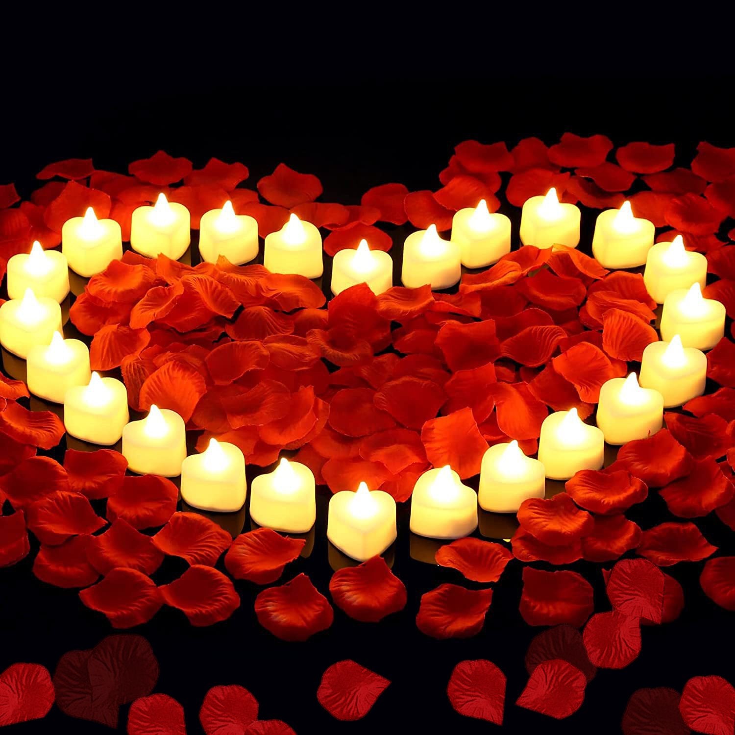 Heart shape made of red rose petals with white LED tea lights inside on a black background