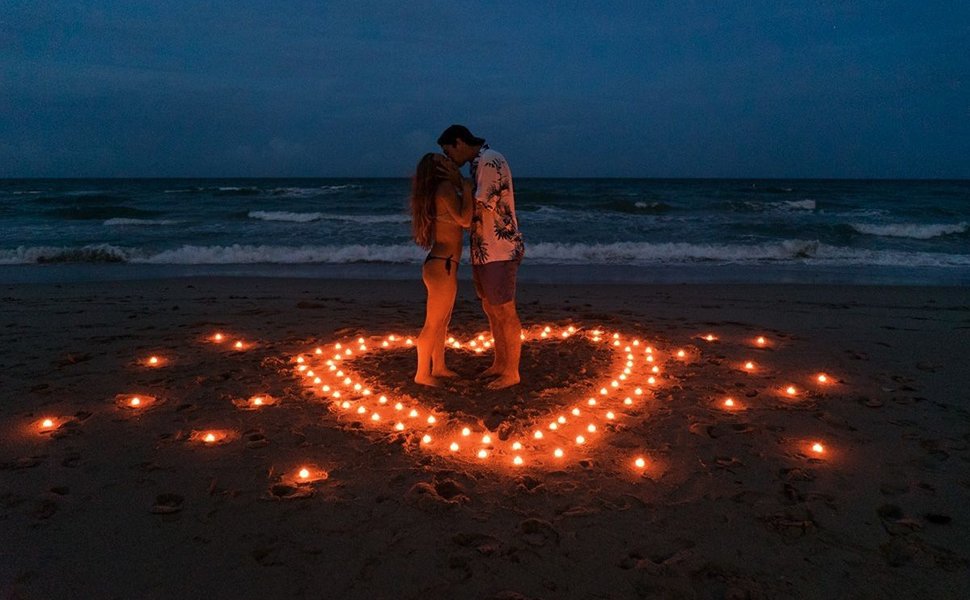 Couple kissing on a beach at night, surrounded by a heart shape made of lit LED tea lights