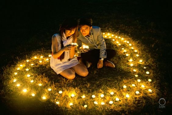 Couple sitting in grass surrounded by heart-shaped arrangement of LED tea lights at night