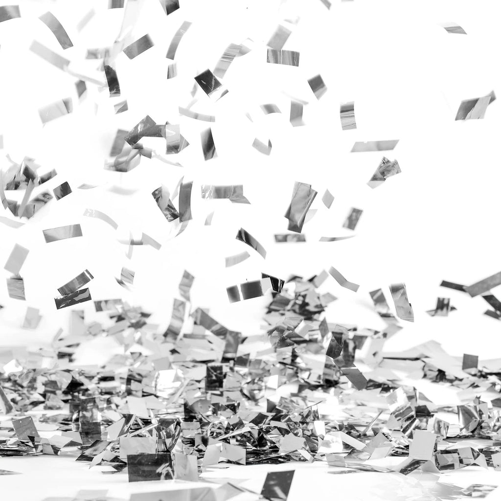 Silver confetti scattered on a white surface with more pieces falling from above.