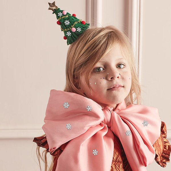 Young girl wearing a festive tree hat and large pink bow, adorned with small metal snowflakes.