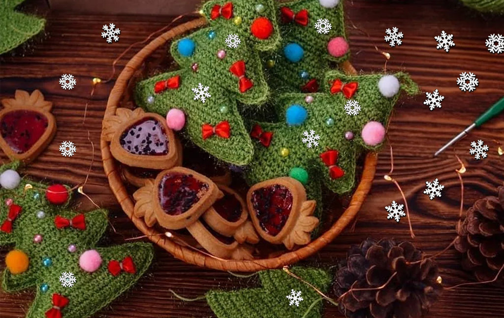 Crocheted Christmas trees and jam-filled cookies arranged on a wooden surface with scattered snowflakes and fairy lights.