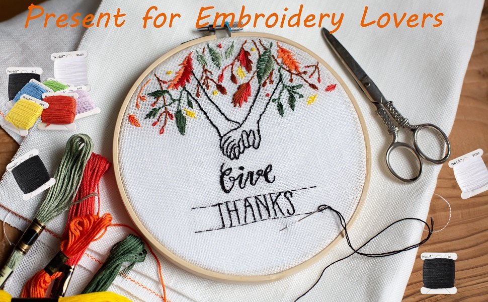 Embroidery hoop with 'Give Thanks' design, surrounded by colorful embroidery floss and scissors.