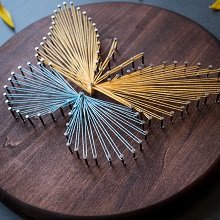 String art butterfly on a wooden circular board, made with gold and blue threads and nails.