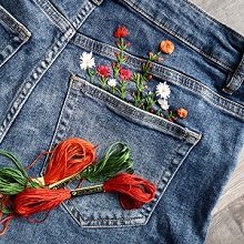 Embroidery floss and stitched flowers in the pocket of blue jeans