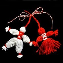 Two handmade yarn dolls, one white and one red, tied with white and red string against a black background.