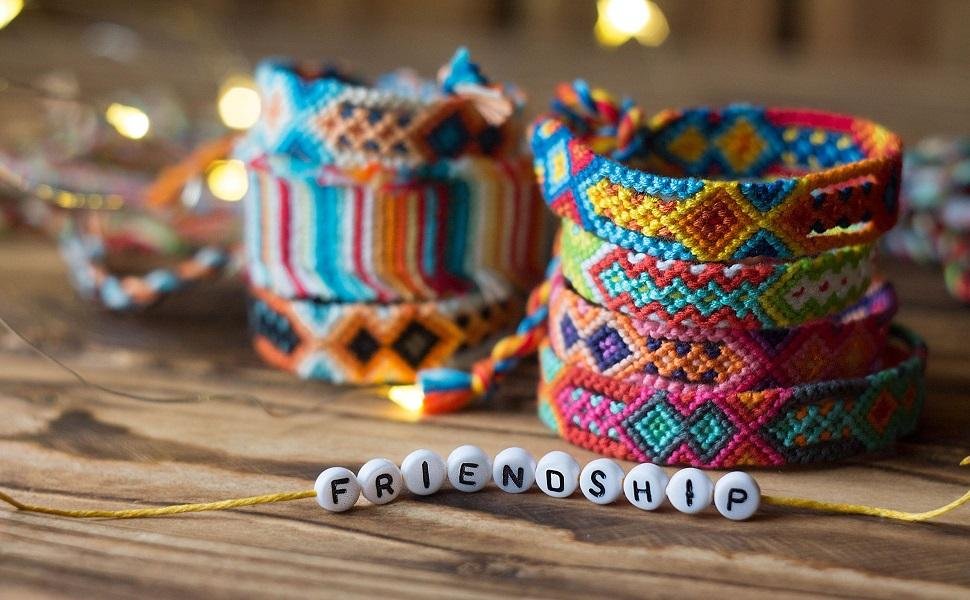 Stacks of colorful woven friendship bracelets with white letter beads spelling out 'FRIENDSHIP' on a wooden surface.