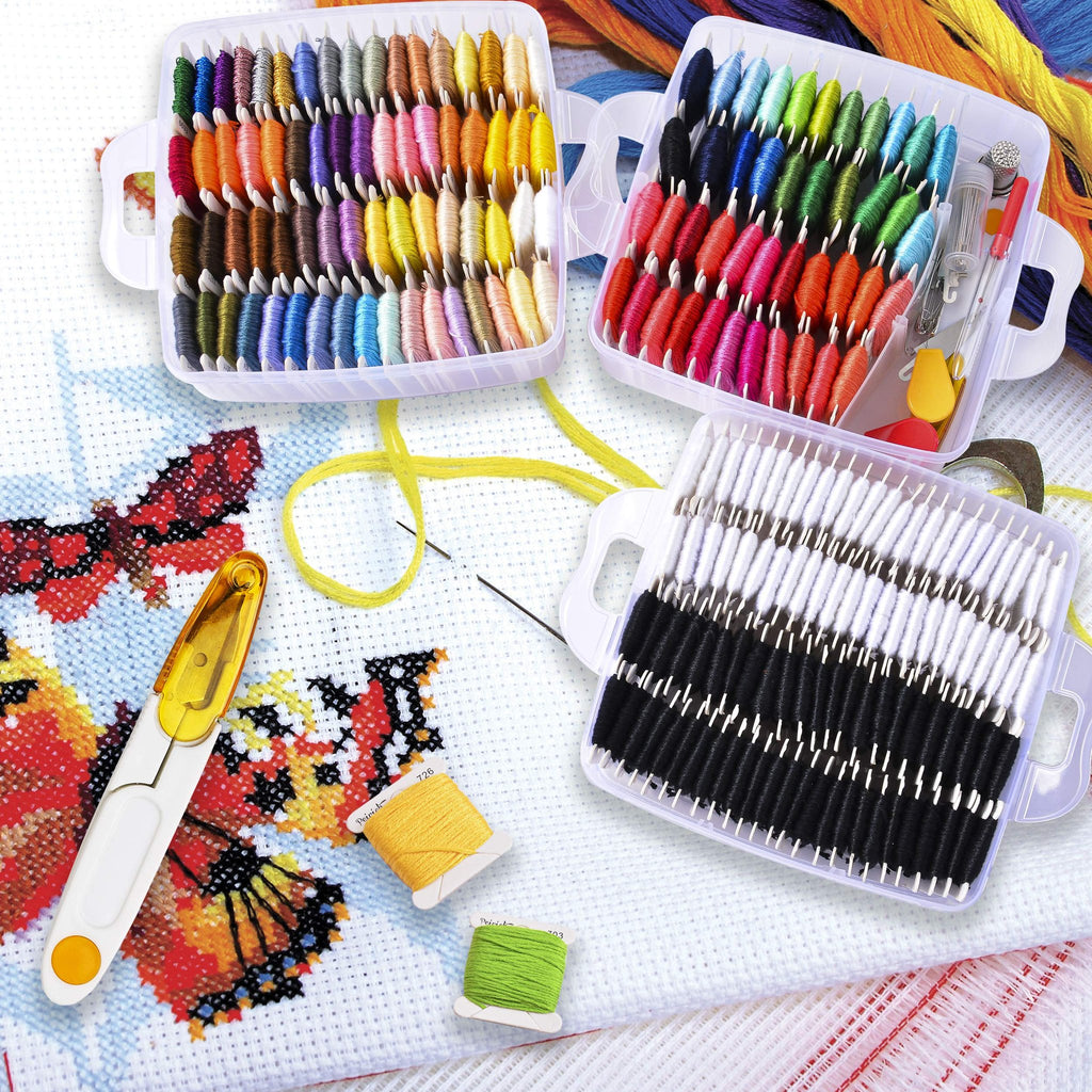 Embroidery floss kit with multiple colors organized in plastic cases, cross-stitch fabric with butterfly design, scissors, needles, and thread spools.