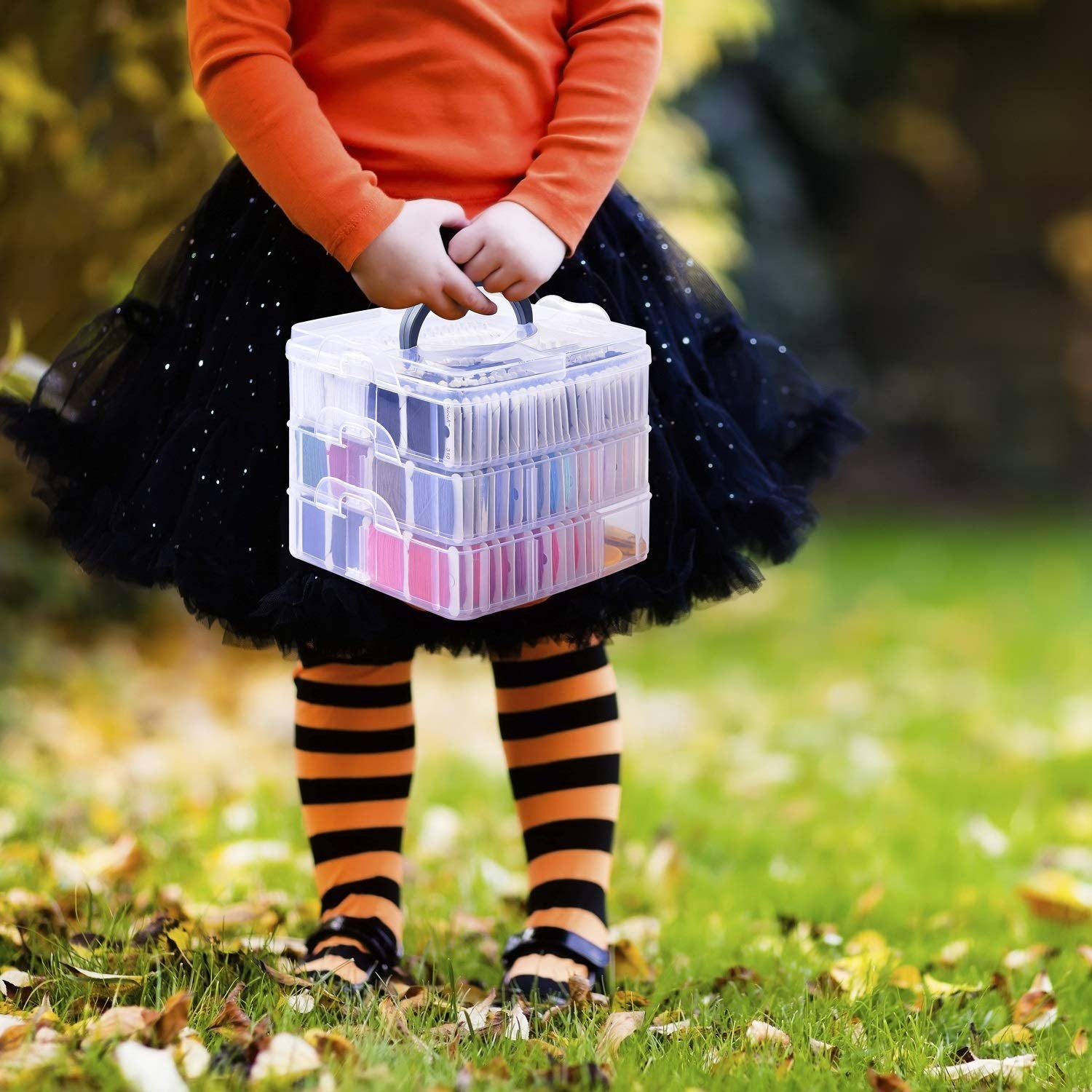 Child in Halloween costume holding a clear organizer box filled with colorful embroidery floss
