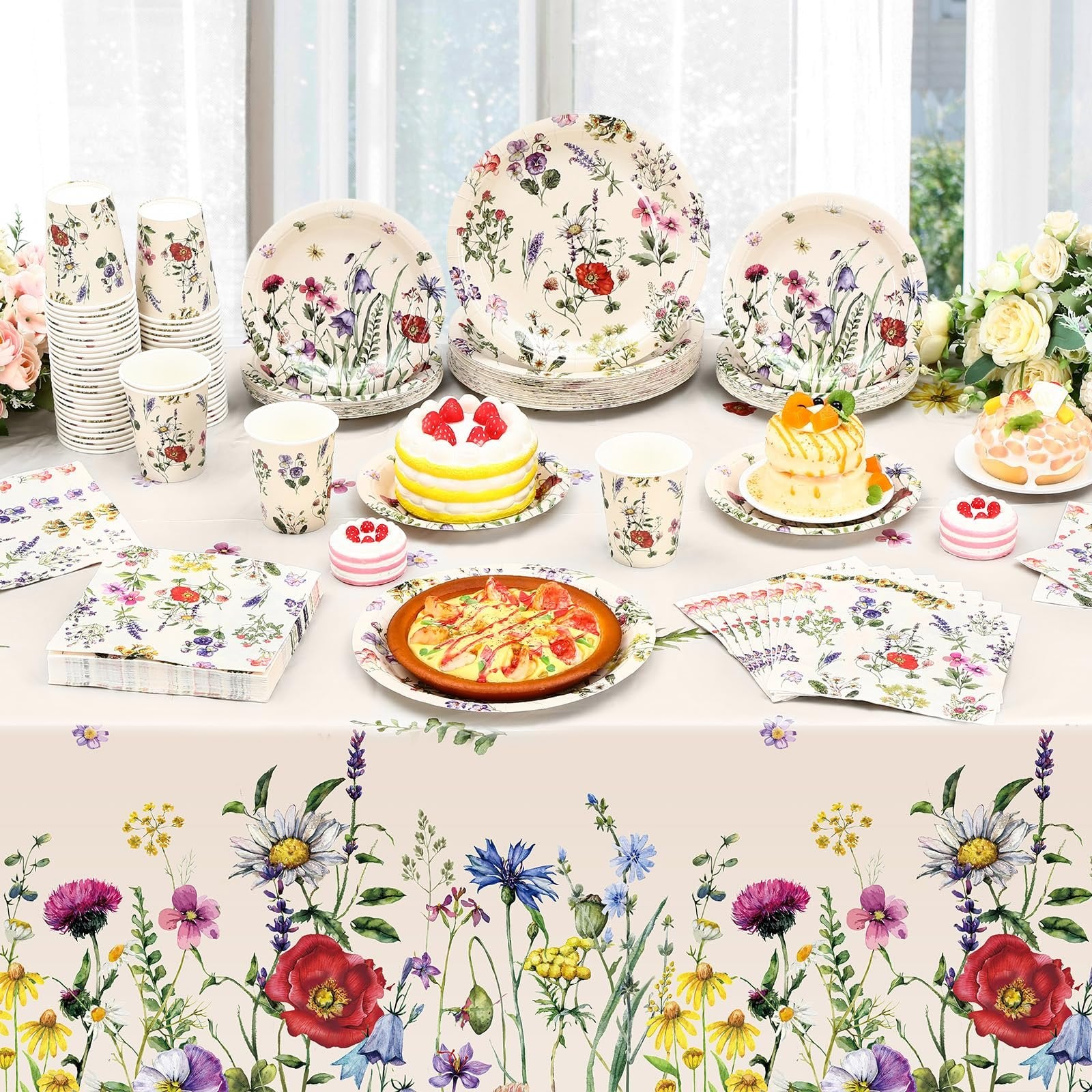 Wildflower party tableware set with plates, cups, napkins, and tablecloth laid out with cakes and pizza.