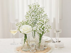 Arrangement of artificial baby's breath flowers in decorative vases on a table setting with a wine glass and candle holder.