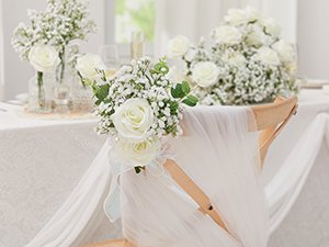 Artificial baby's breath and white rose bouquets decorating a chair at a wedding reception table