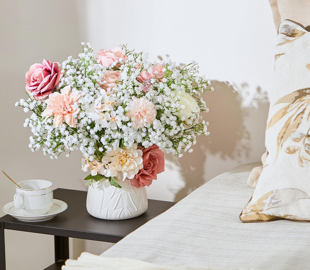 Artificial baby's breath and rose bouquet in a white vase on a side table with a teacup