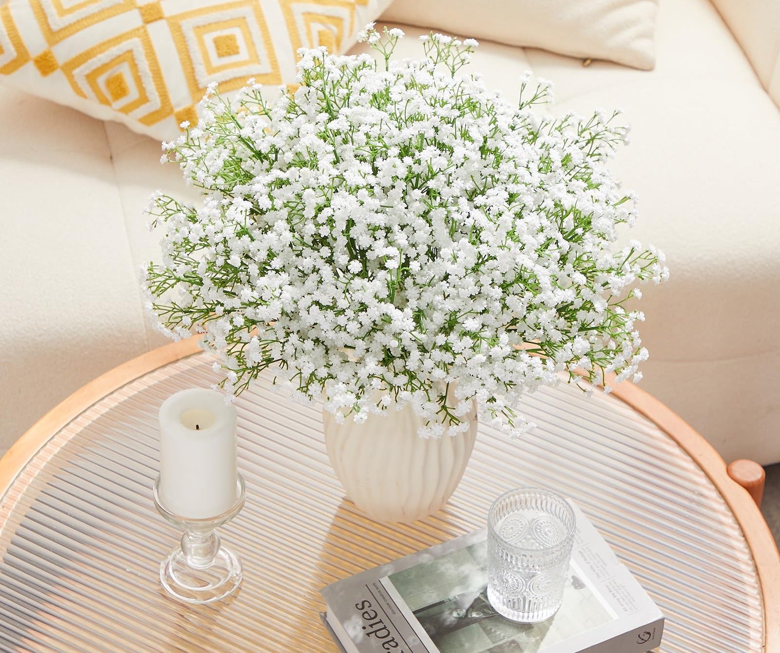Bouquet of artificial baby's breath flowers in a vase on a coffee table with a candle and book.