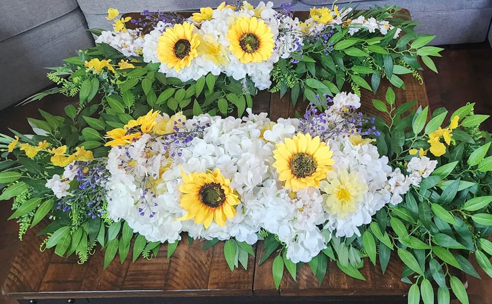 Two floral arrangements with sunflowers, white hydrangeas, and greenery on a wooden table.