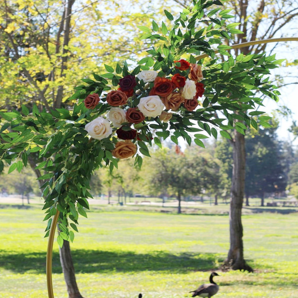 Artificial Italian Ruscus greenery stems with roses on a gold arch in a park setting