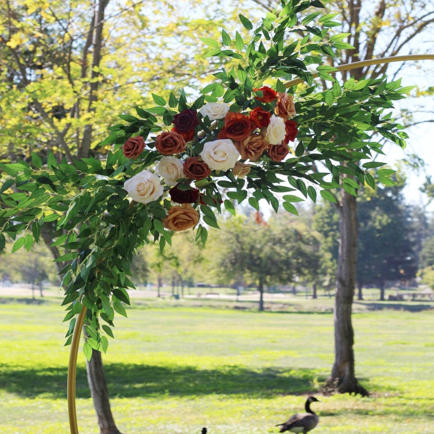 Artificial Italian Ruscus greenery stems with roses on a gold arch in a park setting
