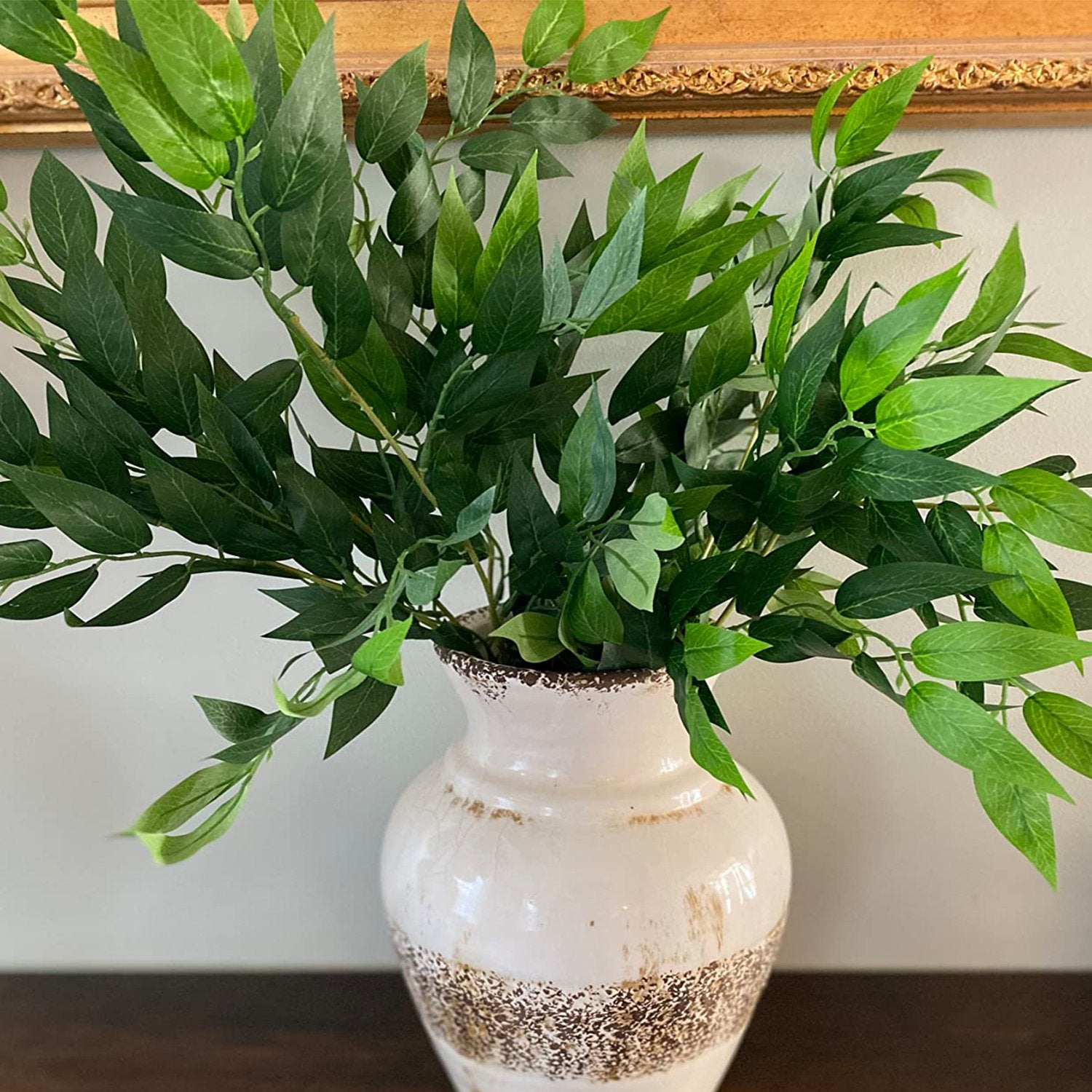 Artificial Italian Ruscus greenery stems in a decorative vase, close-up view.