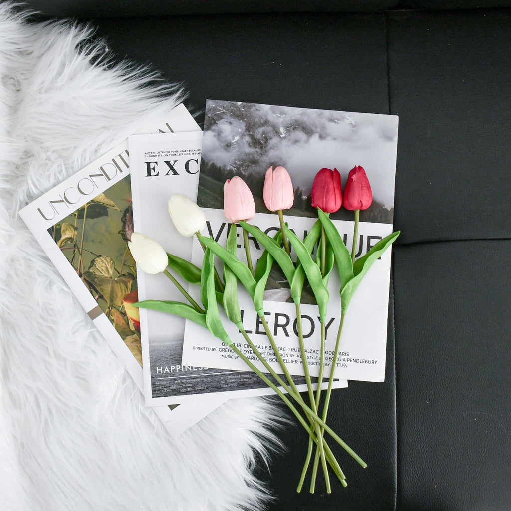 Artificial tulips in shades of pink, red, and white arranged on magazines and faux fur.