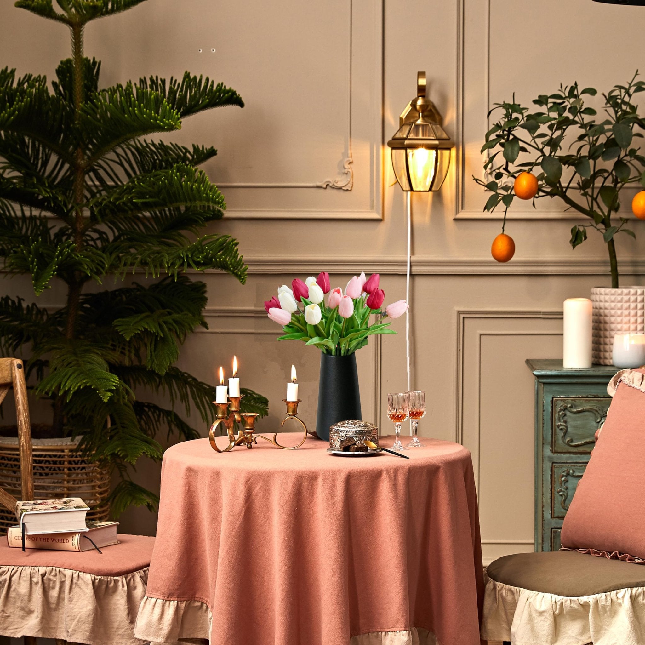 A table set with artificial pink and white tulips in a black vase, books, and candles, creating a cozy vignette.