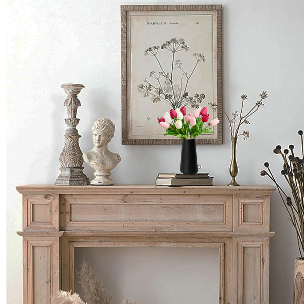 A vase of pink and white artificial tulips sits on a wooden mantelpiece with decorative items.