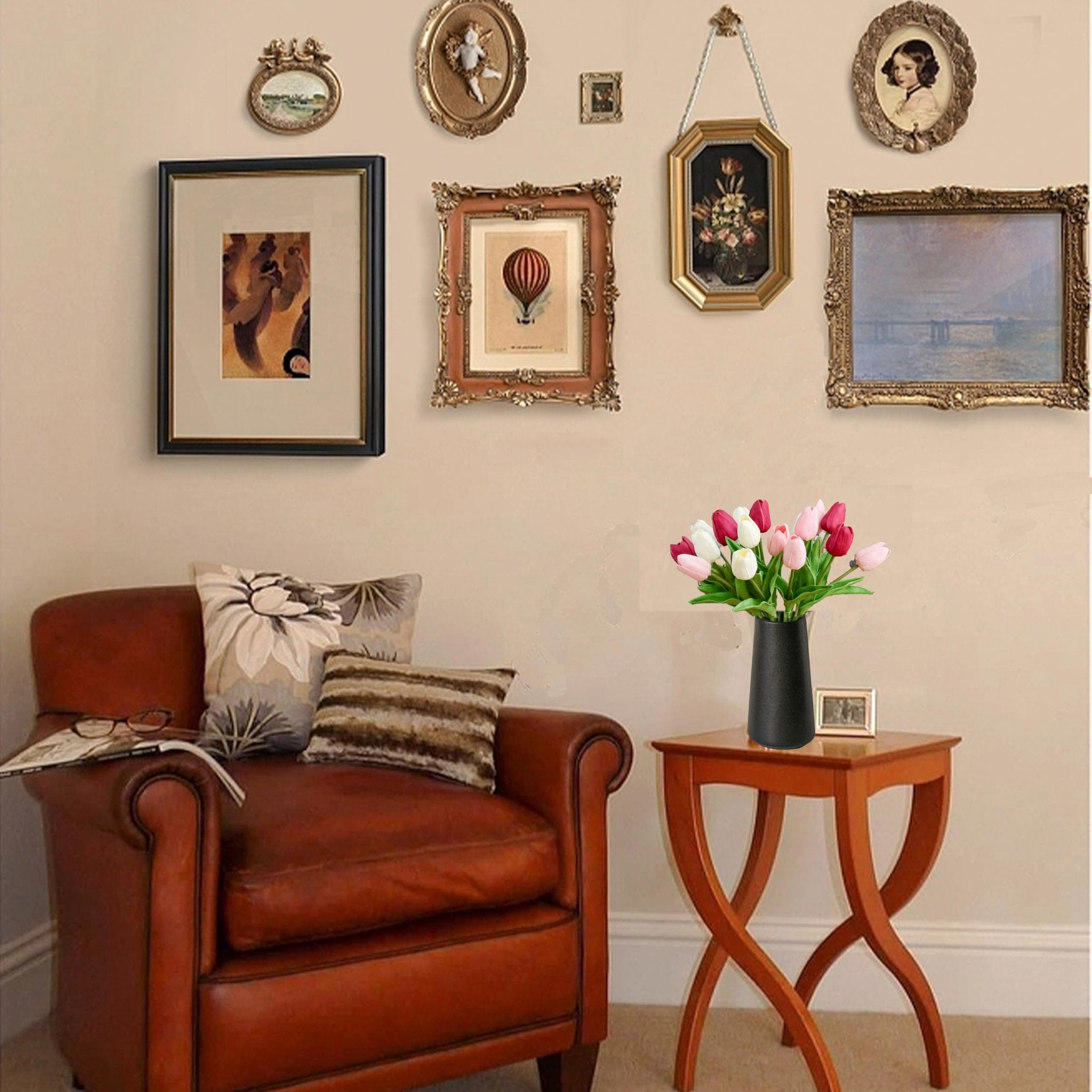 A vase of pink and white artificial tulips sits on a side table next to a leather armchair with a book and glasses.