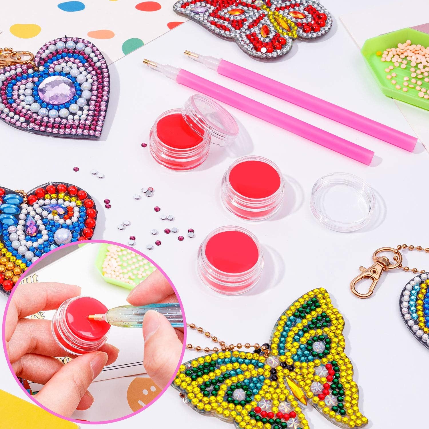 Diamond art keychain kits with pink drills, red wax pots, and tools on a white surface with colorful dots background.