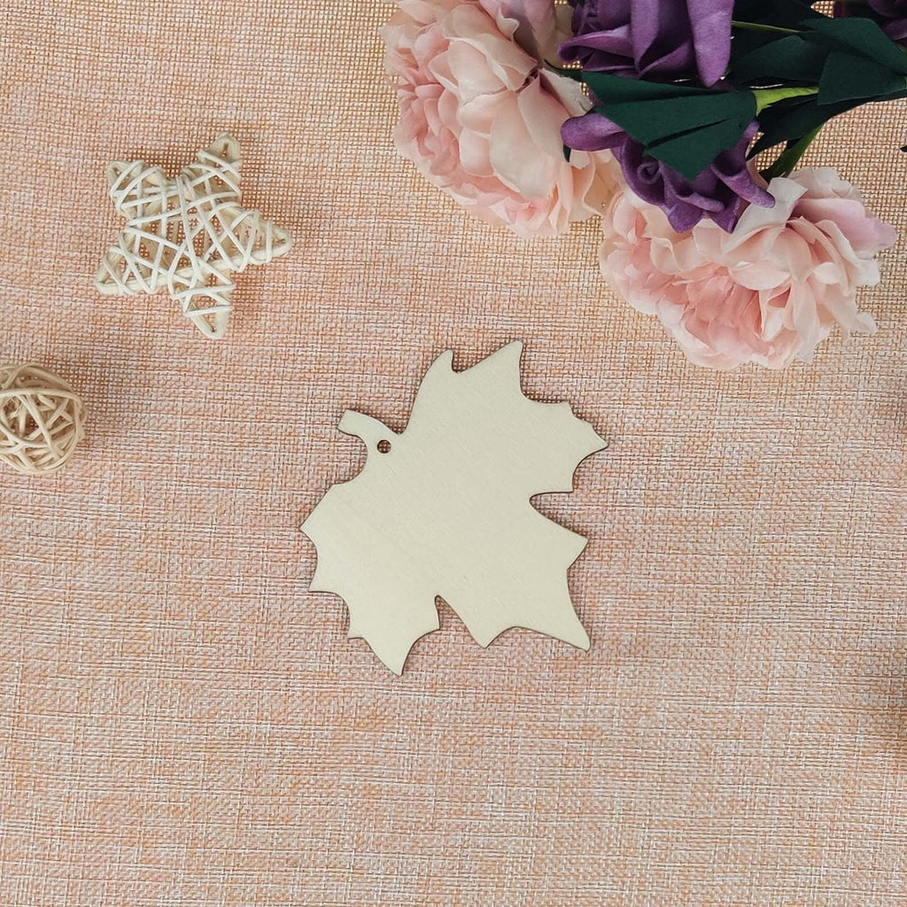 Unfinished wooden maple leaf cutout with a hole for hanging, surrounded by decorative elements like a woven star and flowers.