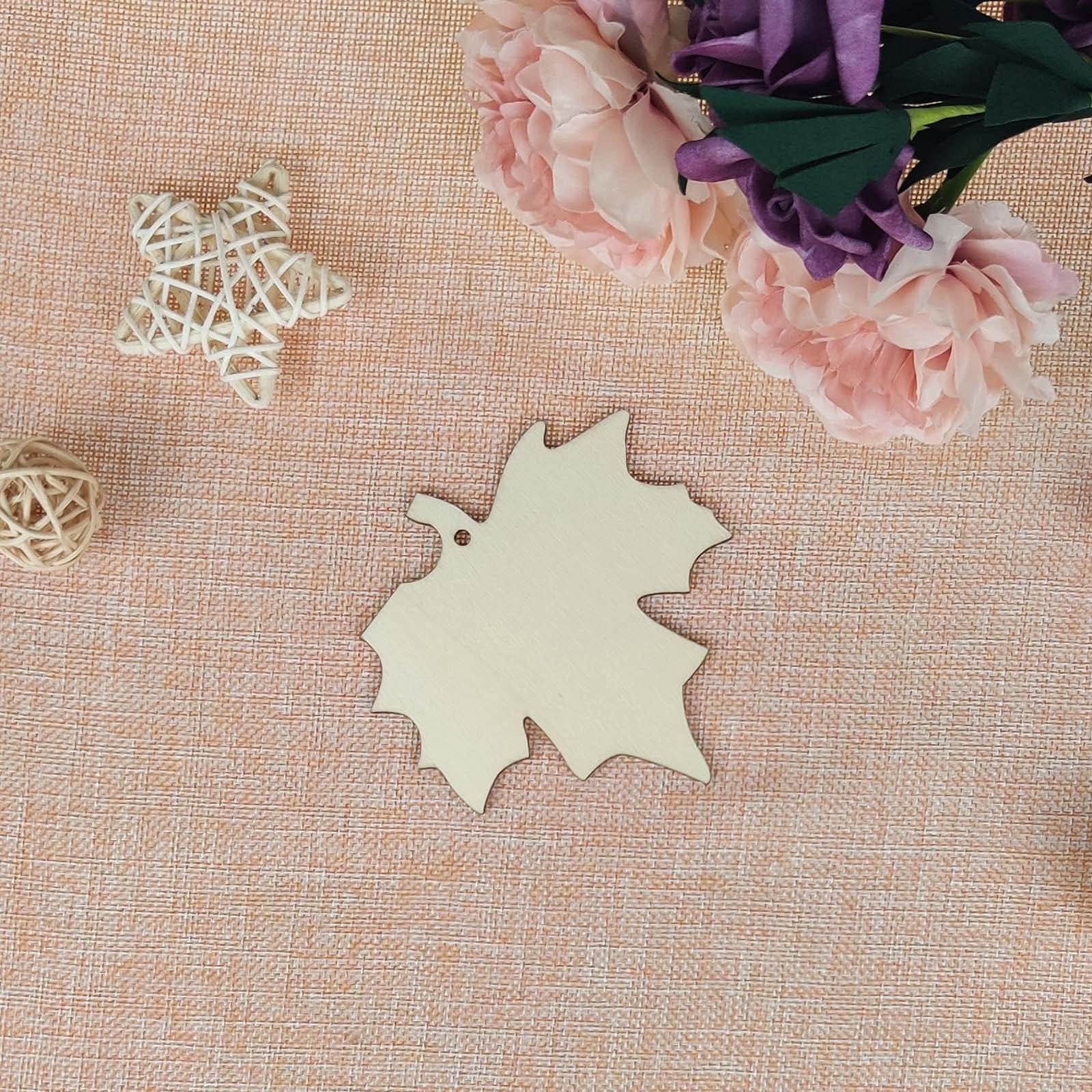 Unfinished wooden maple leaf cutout with a hole for hanging, surrounded by decorative elements like a woven star and flowers.