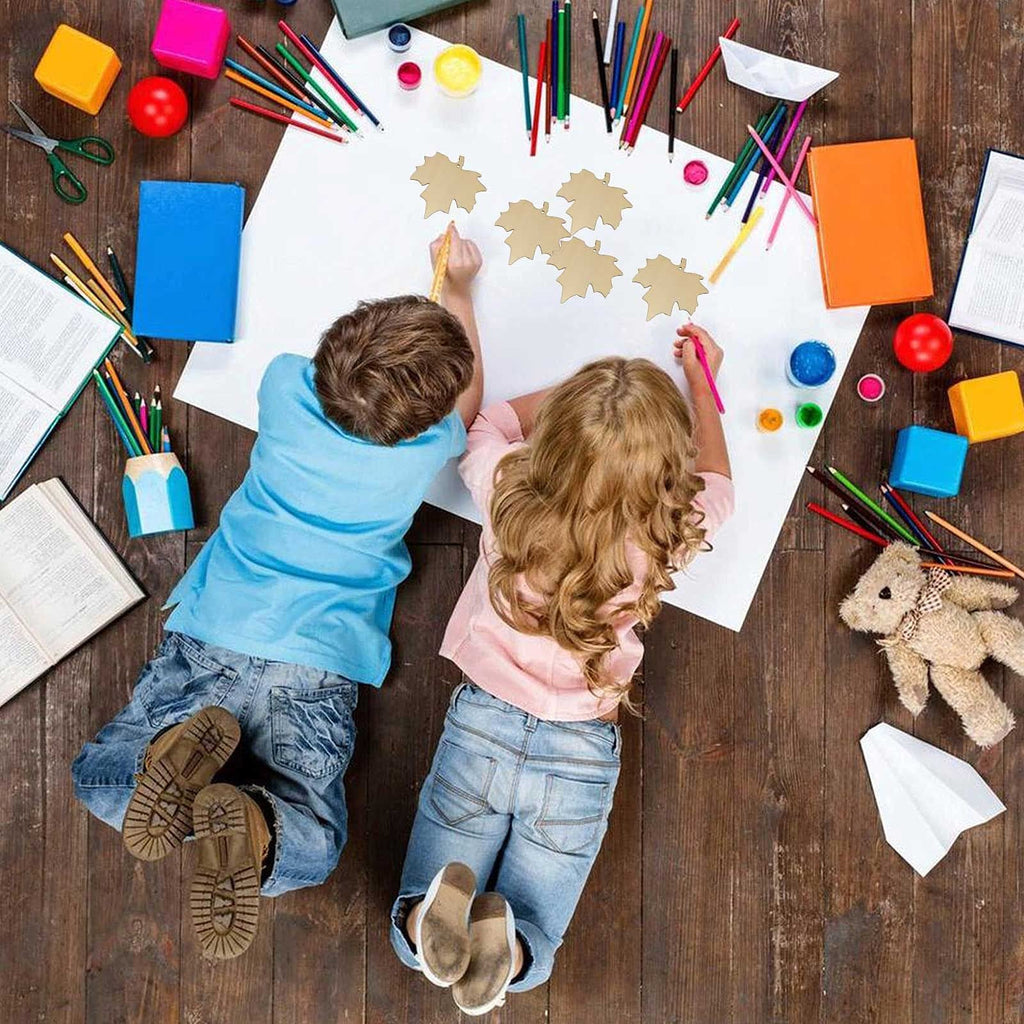 Two children drawing on paper with wooden maple leaf cutouts scattered around