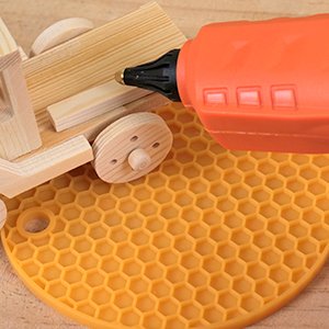 Cordless hot glue gun dispensing glue onto a wooden toy car on a honeycomb mat