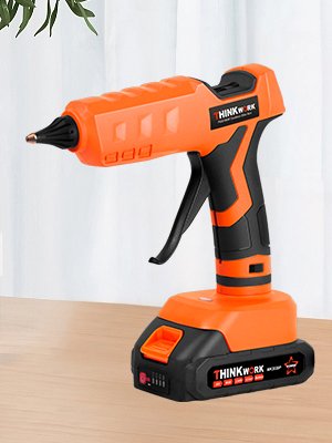 Orange and black cordless hot glue gun with battery pack on a wooden surface.