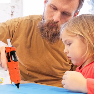 Man and child looking at an orange cordless hot glue gun during a craft project