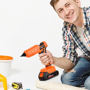 Man holding an orange cordless hot glue gun with a white background and craft supplies