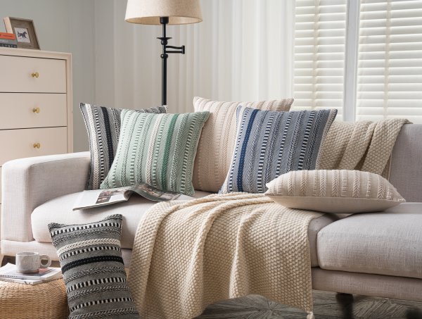 Set of boho throw pillow covers in navy blue, green, and beige with woven stripes arranged on a sofa with a knit blanket.