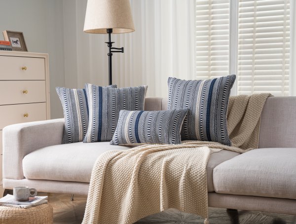 Four navy blue and cream striped throw pillows arranged on a sofa with a beige throw blanket.