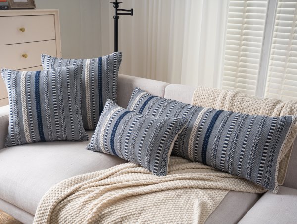 Four boho throw pillow covers with navy blue, white, and grey woven stripes on a sofa with a cream blanket.