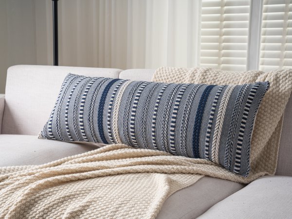 Navy blue and cream striped lumbar pillow cover on a sofa with a cream throw blanket.