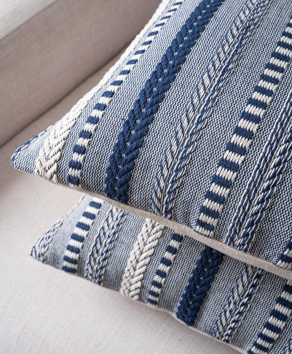 Close-up of two navy blue and white woven throw pillow covers stacked on a textured surface.