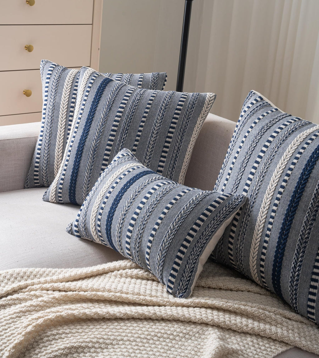 Set of four navy blue and cream boho throw pillow covers with woven stripes on a sofa with a cream blanket.