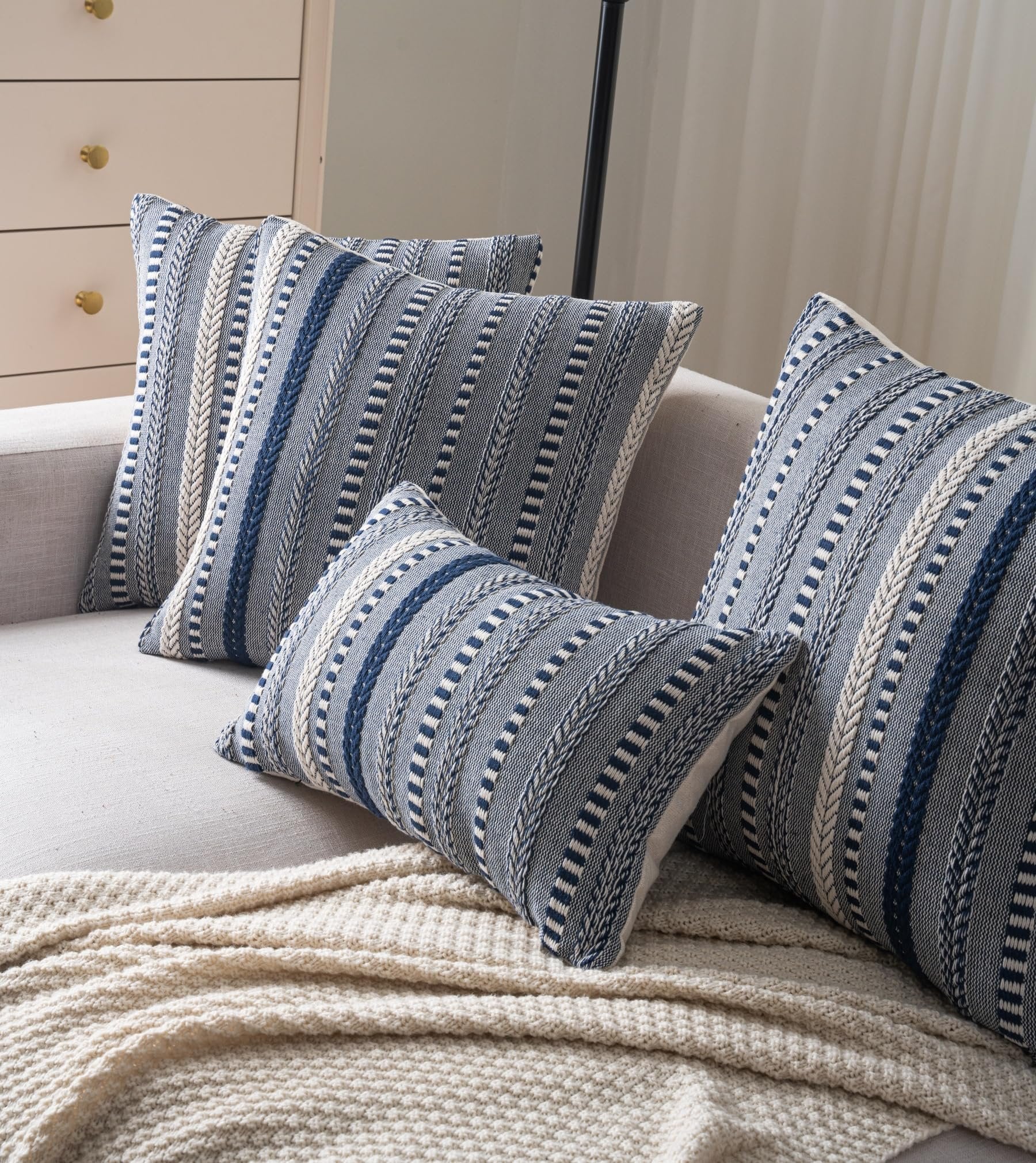 Set of four navy blue and cream boho throw pillow covers with woven stripes on a sofa with a cream blanket.