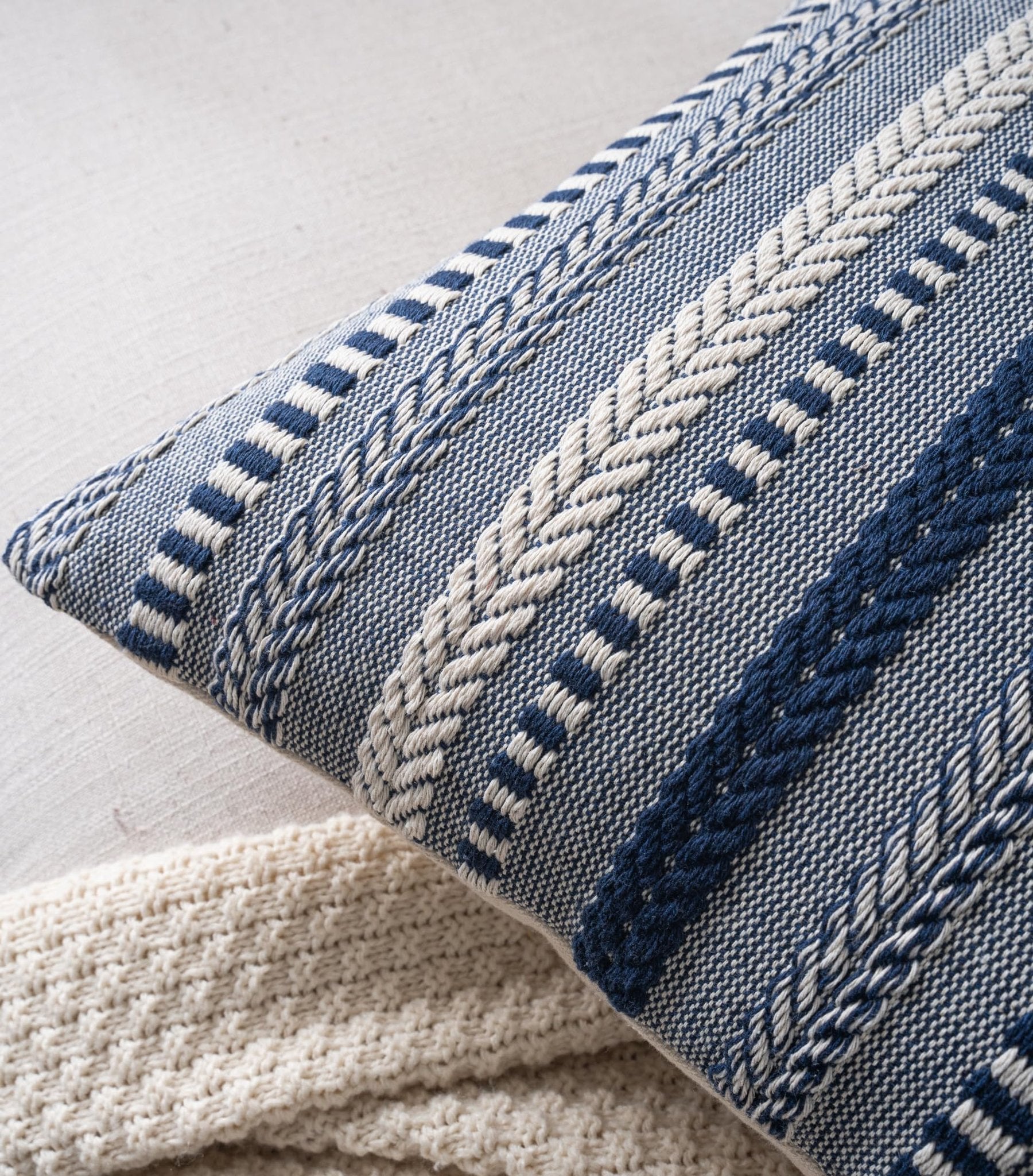 Close-up of a navy blue and white woven throw pillow cover with textured stripes and a cream knit blanket.