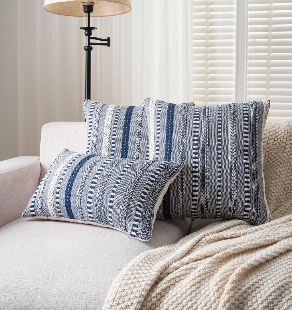 Three navy blue and white striped boho throw pillow covers arranged on a sofa with a cream knit blanket.