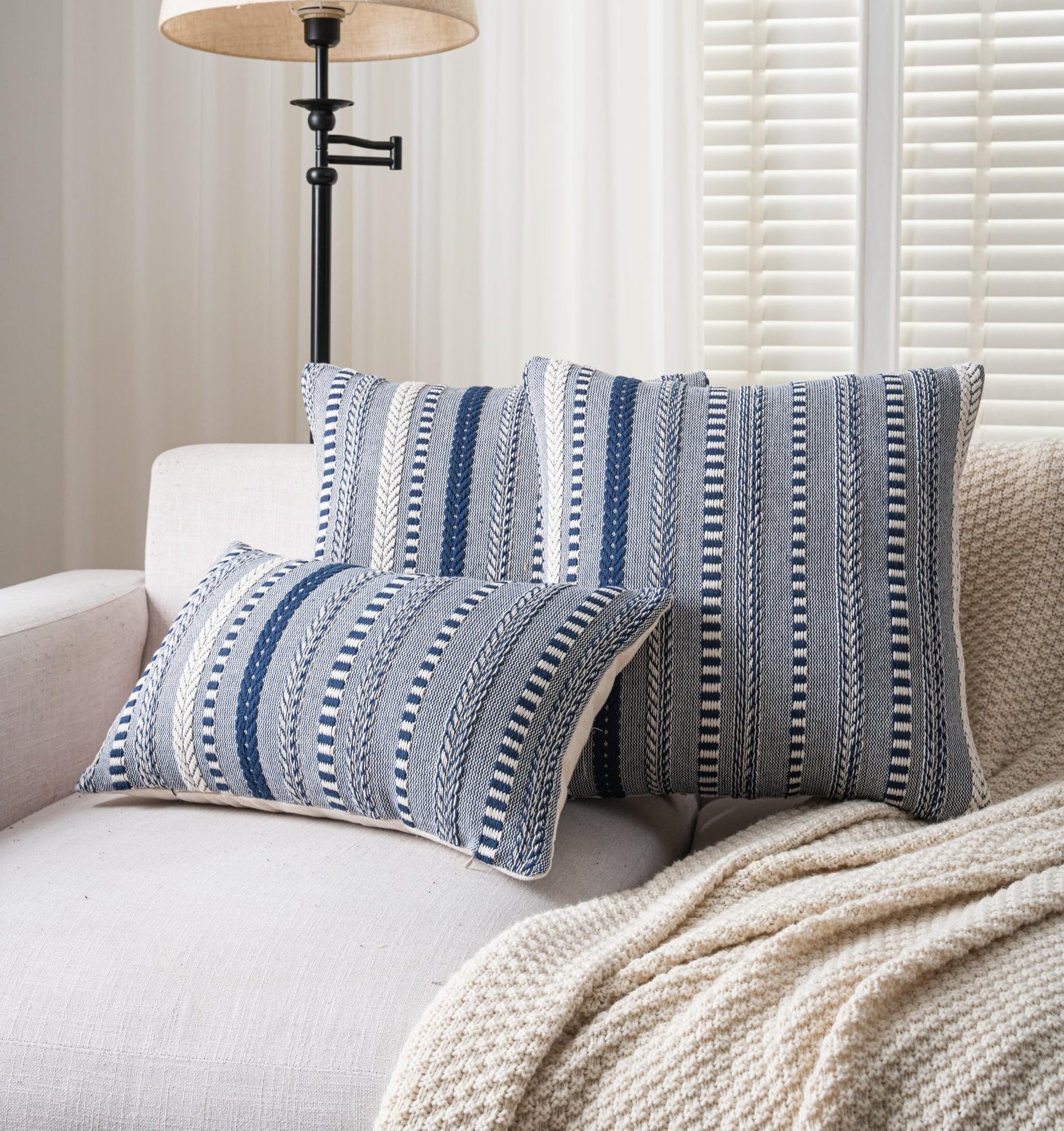 Three navy blue and white striped boho throw pillow covers arranged on a sofa with a cream knit blanket.