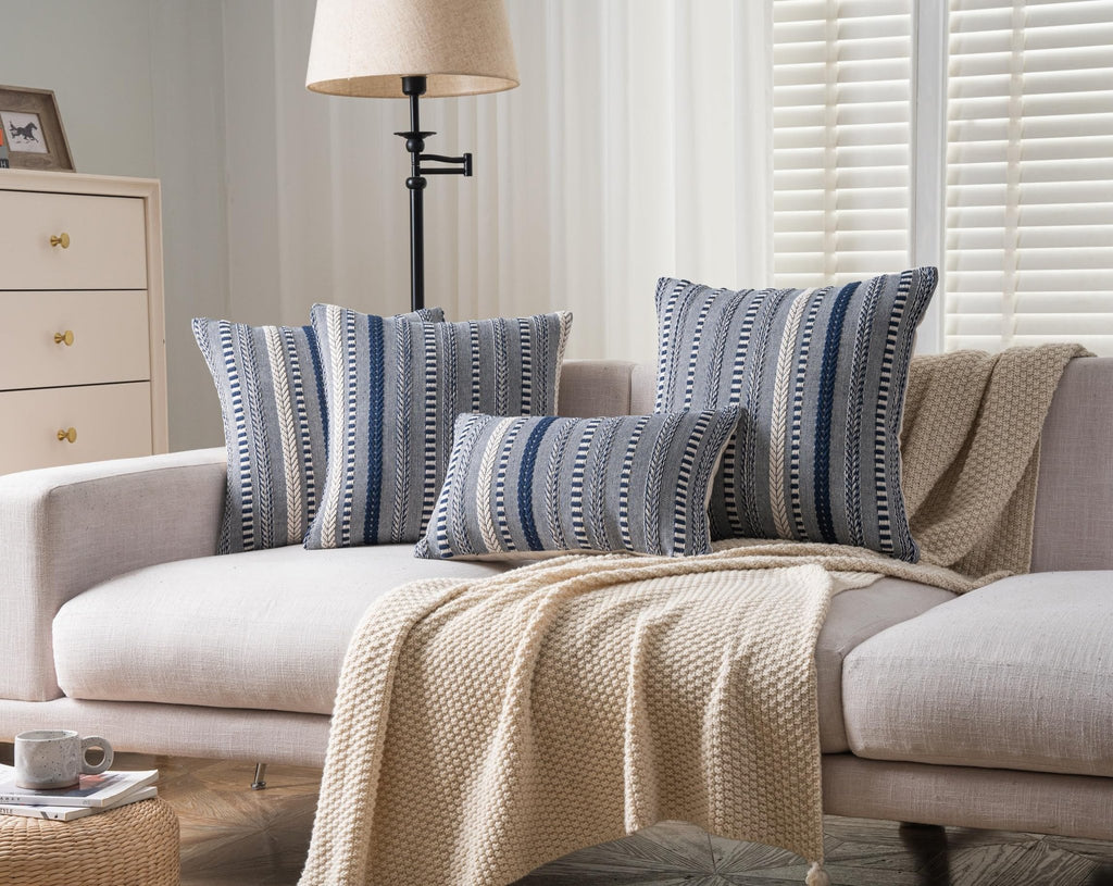 Four boho throw pillows with navy blue and white woven stripes on a sofa with a cream knit blanket.