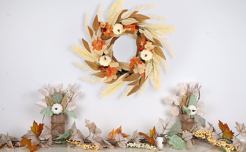 Artificial fall wreath with white pumpkins, orange flowers, and autumn leaves, displayed above a garland and two small floral arrangements.